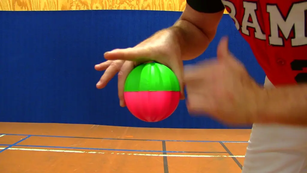 A pitcher holding an EZ-Riseball, green hemisphere over magenta, the moulded ribs running under the fingers